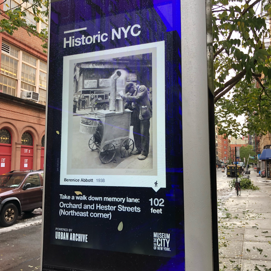 Kiosk on a sidewalk showing a historical photo from Museum of the City of New York.