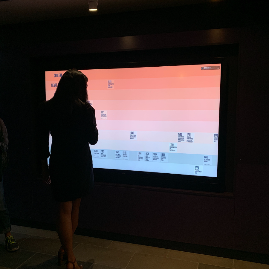 A person standing in front of a large touchscreen that displays an interactive historical timeline.