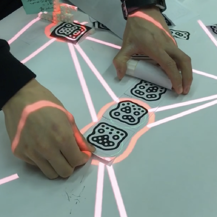 Hands arranging printed paper squares on a table, with lines of light connecting them.
